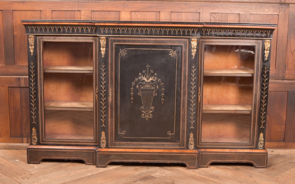 A Victorian ebonised breakfront credenza featuring glazed side doors, gilt incised urn motifs, and cast decorative mounts. View II