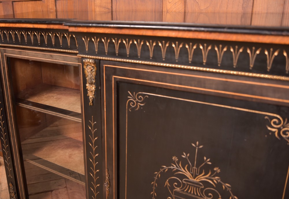 A Victorian ebonised breakfront credenza featuring glazed side doors, gilt incised urn motifs, and cast decorative mounts. View III