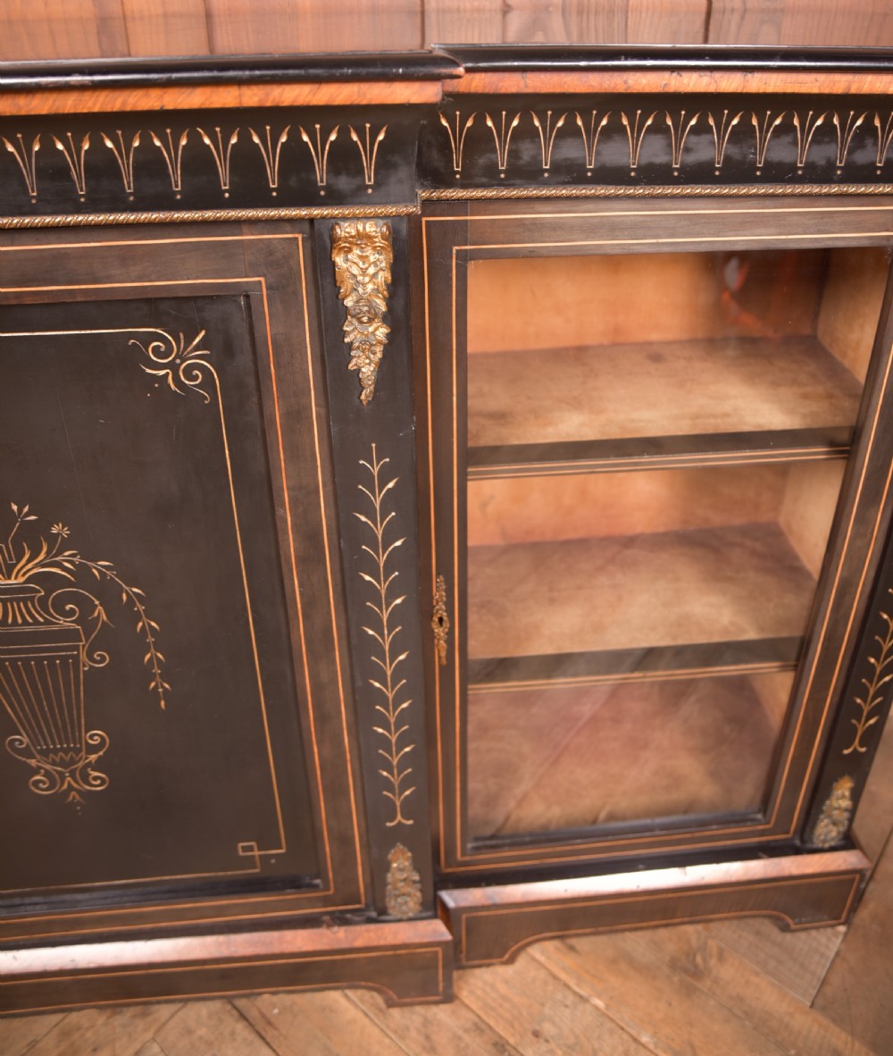 A Victorian ebonised breakfront credenza featuring glazed side doors, gilt incised urn motifs, and cast decorative mounts. View V