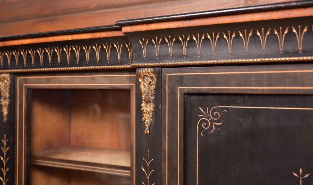 A Victorian ebonised breakfront credenza featuring glazed side doors, gilt incised urn motifs, and cast decorative mounts. View VII