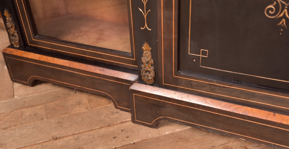 A Victorian ebonised breakfront credenza featuring glazed side doors, gilt incised urn motifs, and cast decorative mounts. View IX