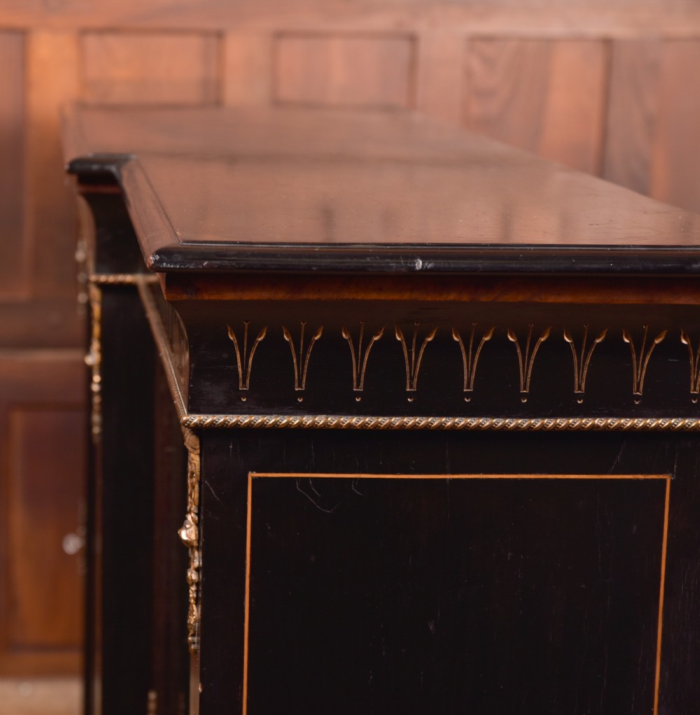 A Victorian ebonised breakfront credenza featuring glazed side doors, gilt incised urn motifs, and cast decorative mounts. View XII
