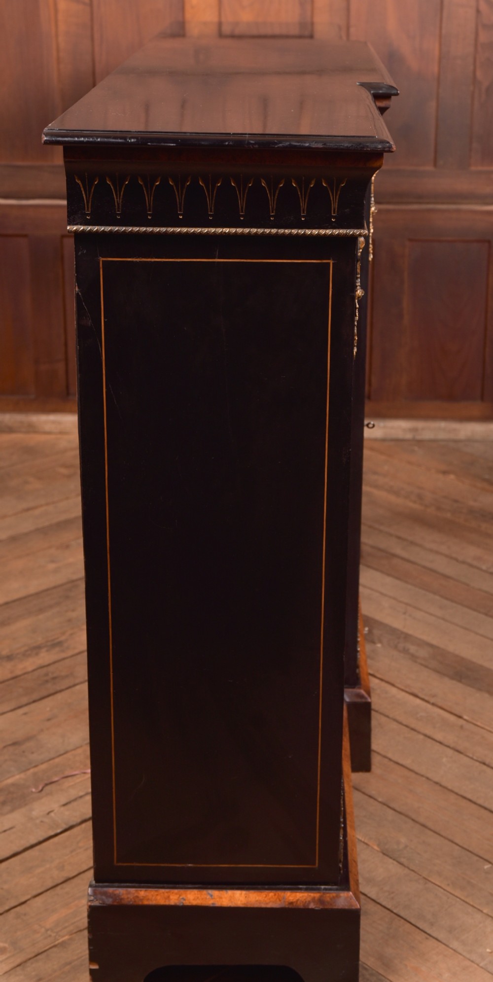 A Victorian ebonised breakfront credenza featuring glazed side doors, gilt incised urn motifs, and cast decorative mounts. View XVI