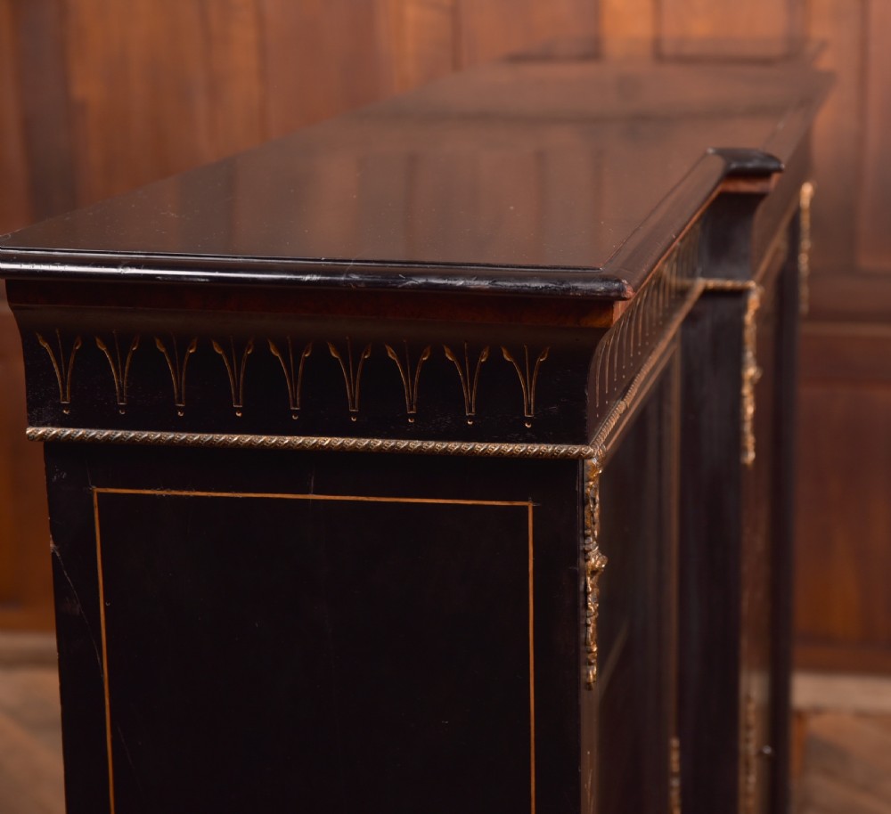 A Victorian ebonised breakfront credenza featuring glazed side doors, gilt incised urn motifs, and cast decorative mounts. View XVII
