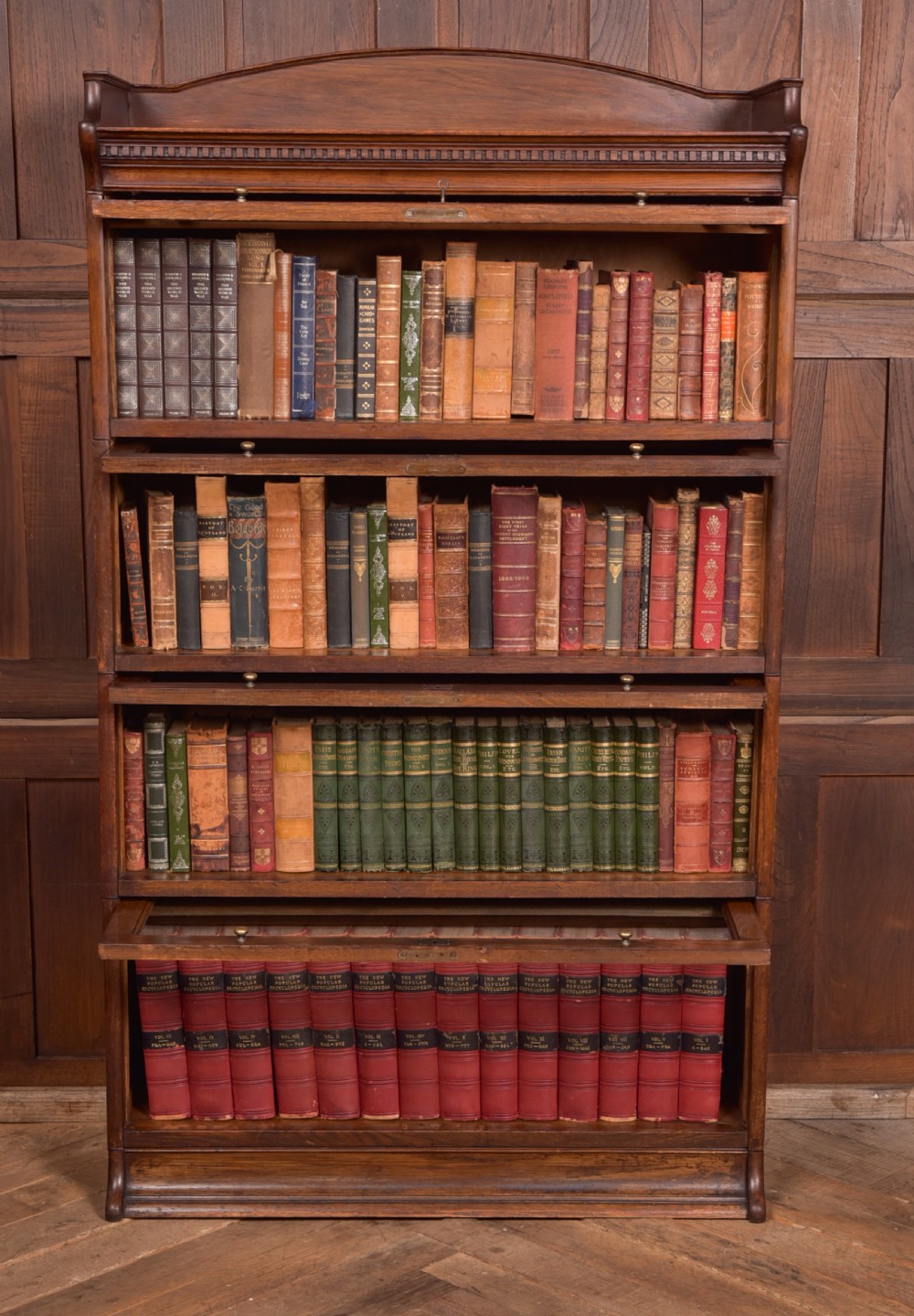 A four-tier dark oak sectional bookcase featuring glass front doors, brass hardware, and a decorative gallery top. View III