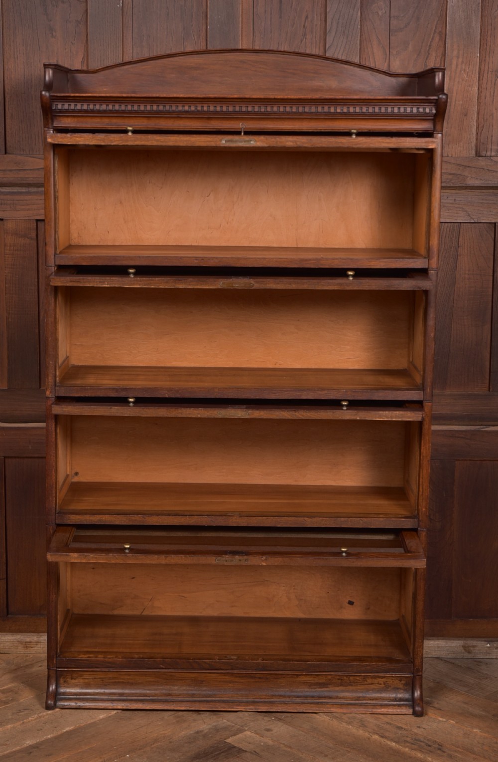 A four-tier dark oak sectional bookcase featuring glass front doors, brass hardware, and a decorative gallery top. View IX