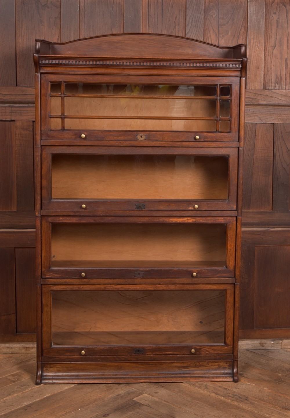 A four-tier dark oak sectional bookcase featuring glass front doors, brass hardware, and a decorative gallery top. View XII