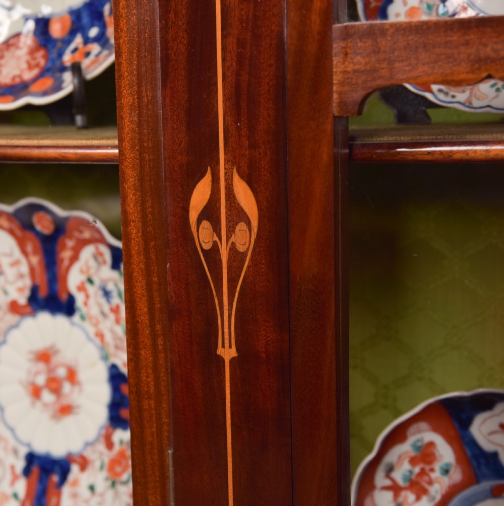 An Art Nouveau mahogany display cabinet featuring stylised floral marquetry inlays, glazed doors, an open upper gallery, and a lower shelf. View II