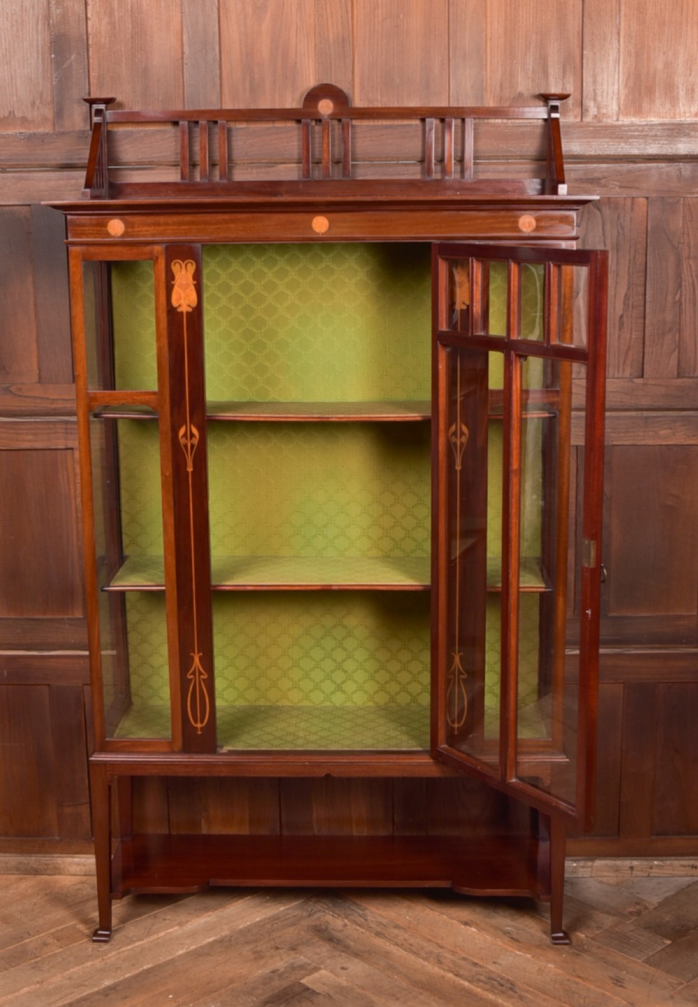 An Art Nouveau mahogany display cabinet featuring stylised floral marquetry inlays, glazed doors, an open upper gallery, and a lower shelf. View VI