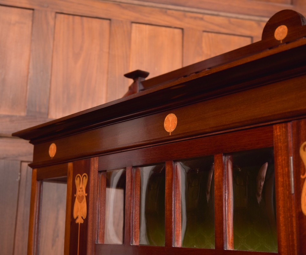 An Art Nouveau mahogany display cabinet featuring stylised floral marquetry inlays, glazed doors, an open upper gallery, and a lower shelf. View XI