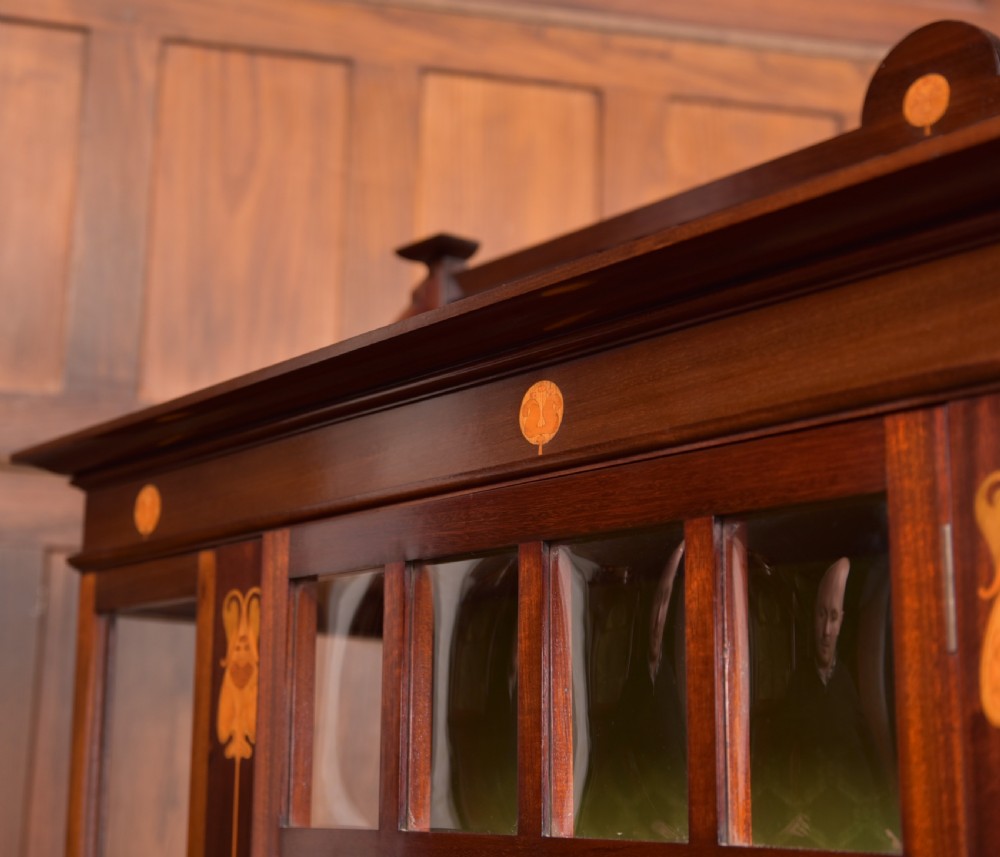 An Art Nouveau mahogany display cabinet featuring stylised floral marquetry inlays, glazed doors, an open upper gallery, and a lower shelf. View XII