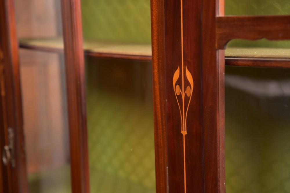An Art Nouveau mahogany display cabinet featuring stylised floral marquetry inlays, glazed doors, an open upper gallery, and a lower shelf. View XV