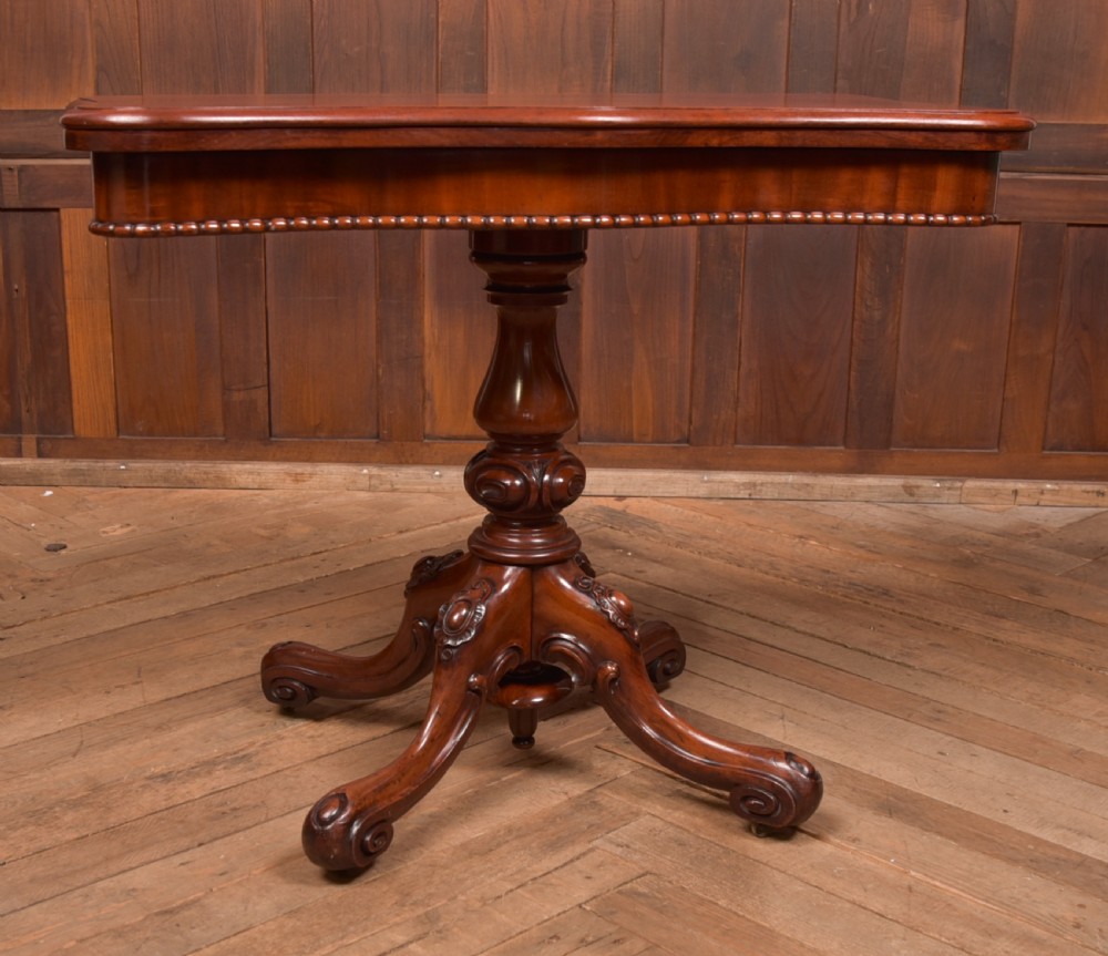 A Victorian mahogany fold-over tea table featuring a serpentine top, bead moulding along the apron, a turned central column, and carved quadruped scroll legs. View II