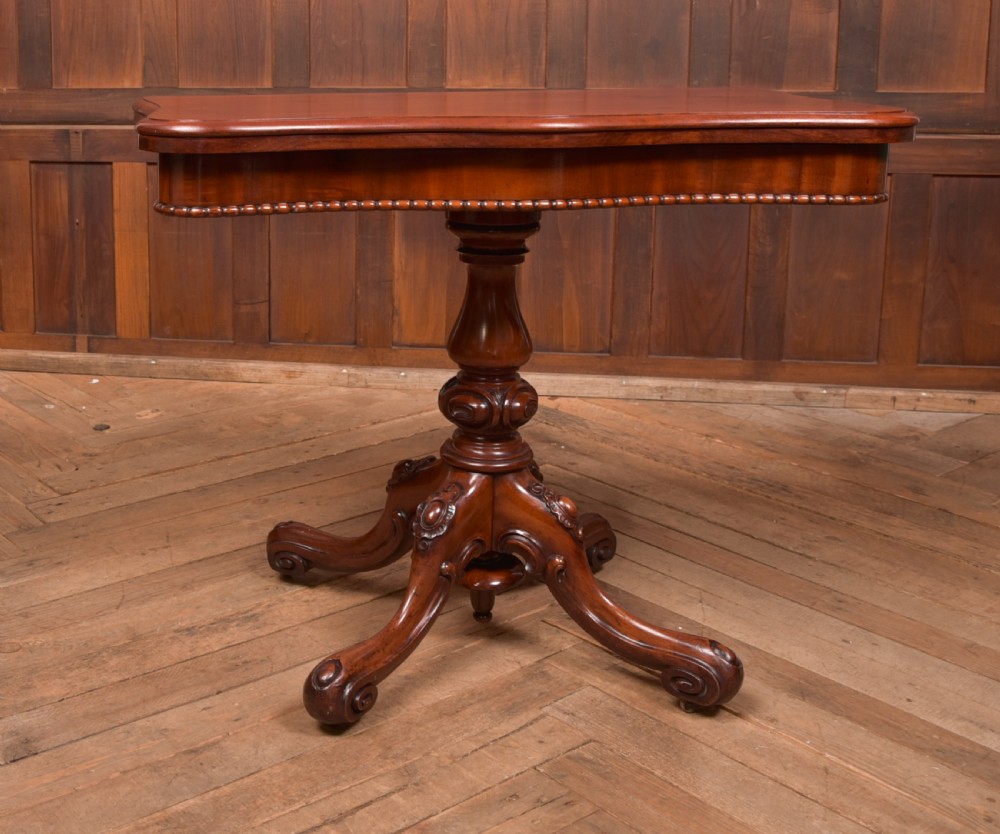 A Victorian mahogany fold-over tea table featuring a serpentine top, bead moulding along the apron, a turned central column, and carved quadruped scroll legs. View III