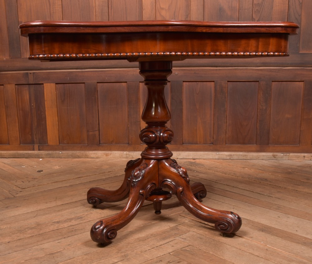 A Victorian mahogany fold-over tea table featuring a serpentine top, bead moulding along the apron, a turned central column, and carved quadruped scroll legs. View V