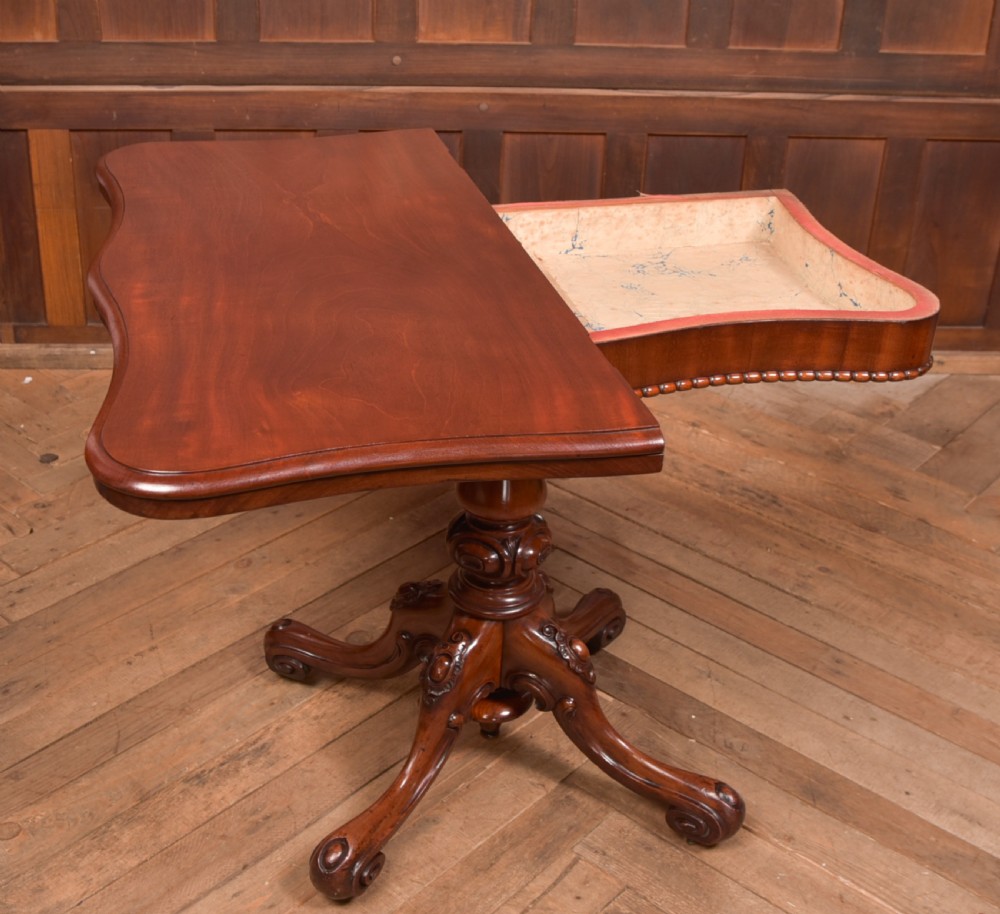 A Victorian mahogany fold-over tea table featuring a serpentine top, bead moulding along the apron, a turned central column, and carved quadruped scroll legs. View VI