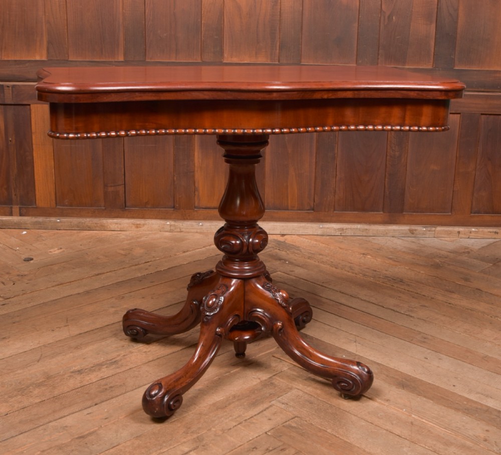 A Victorian mahogany fold-over tea table featuring a serpentine top, bead moulding along the apron, a turned central column, and carved quadruped scroll legs. View VIII