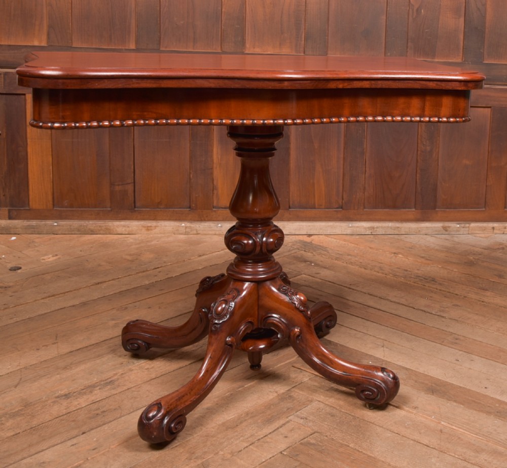 A Victorian mahogany fold-over tea table featuring a serpentine top, bead moulding along the apron, a turned central column, and carved quadruped scroll legs. View IX