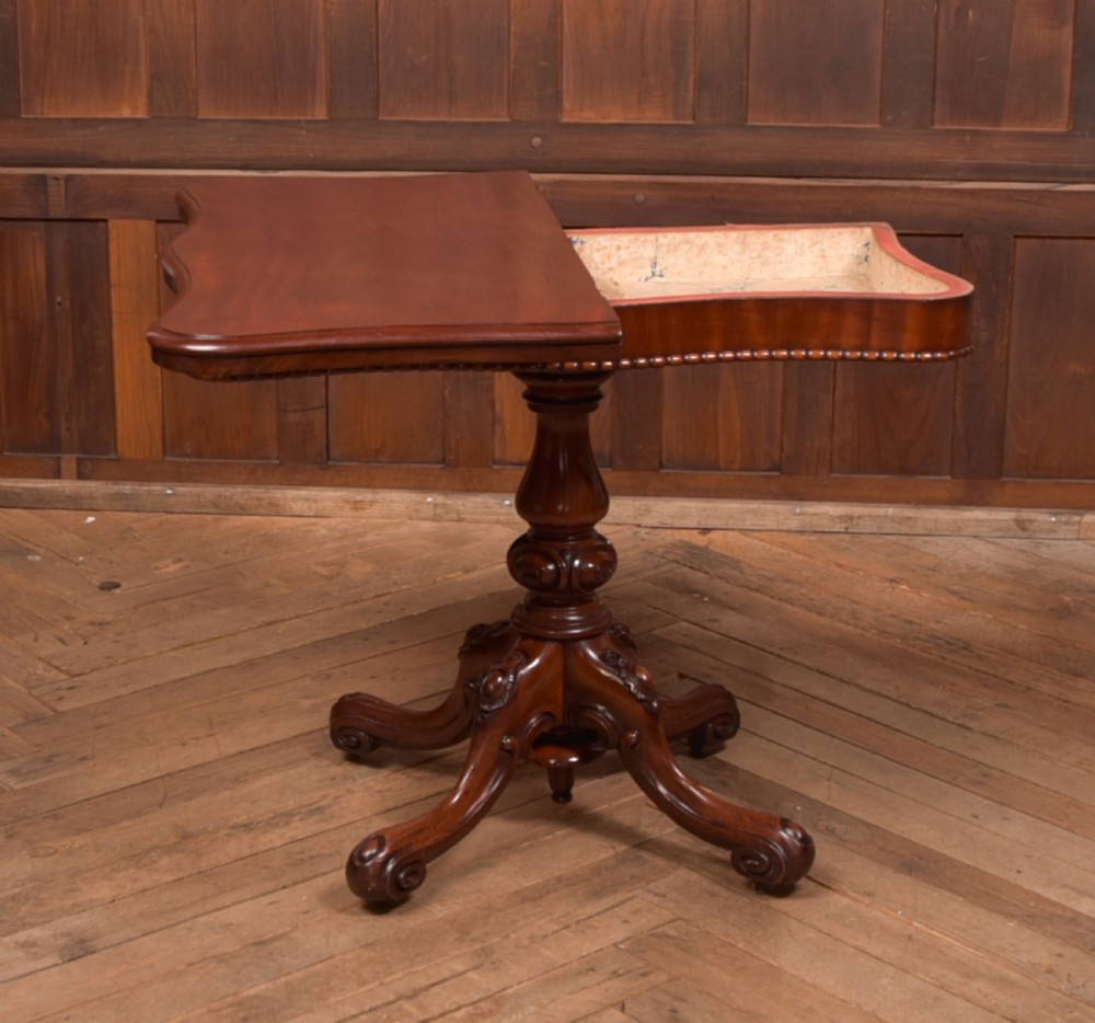 A Victorian mahogany fold-over tea table featuring a serpentine top, bead moulding along the apron, a turned central column, and carved quadruped scroll legs. View X