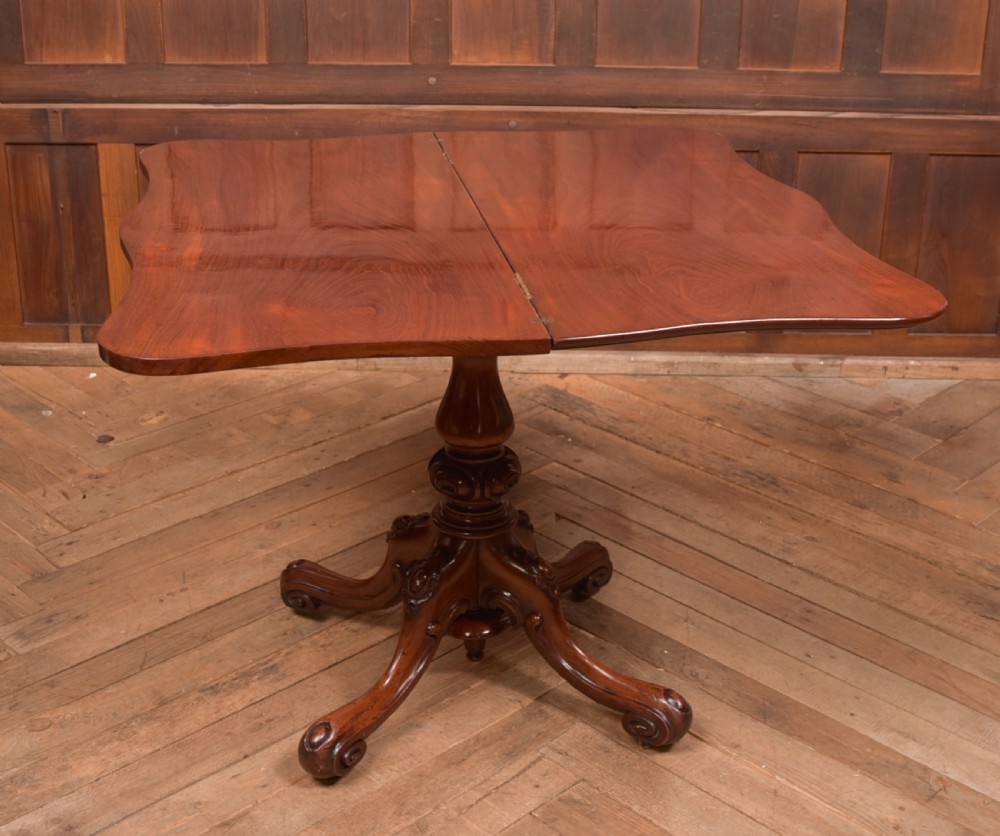 A Victorian mahogany fold-over tea table featuring a serpentine top, bead moulding along the apron, a turned central column, and carved quadruped scroll legs. View XI