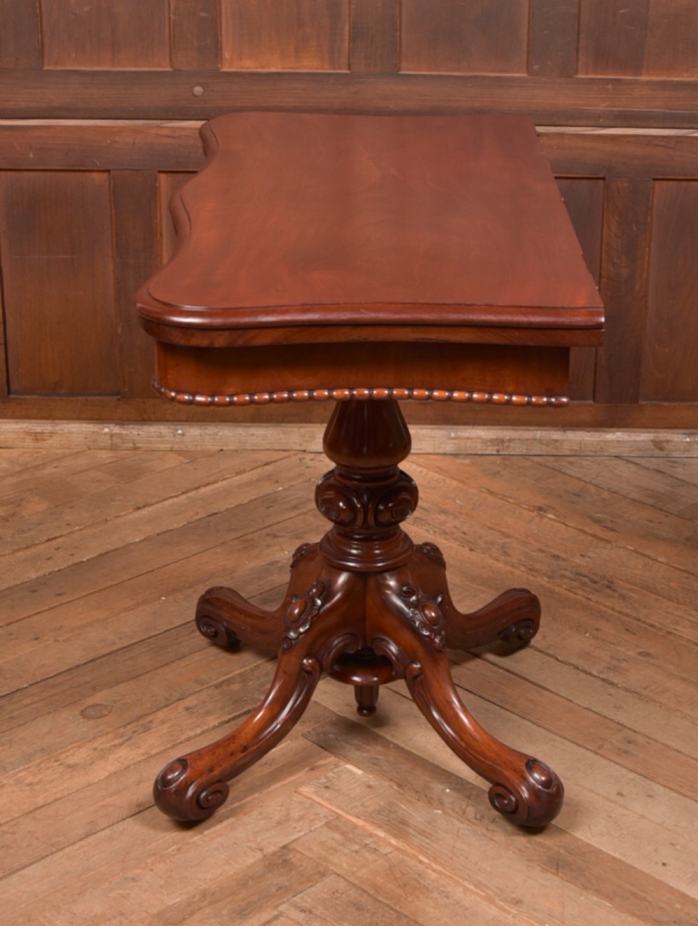 A Victorian mahogany fold-over tea table featuring a serpentine top, bead moulding along the apron, a turned central column, and carved quadruped scroll legs. View XII