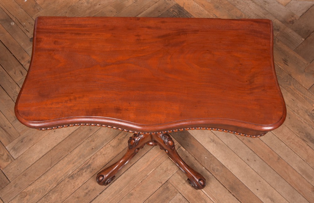 A Victorian mahogany fold-over tea table featuring a serpentine top, bead moulding along the apron, a turned central column, and carved quadruped scroll legs. View XVI