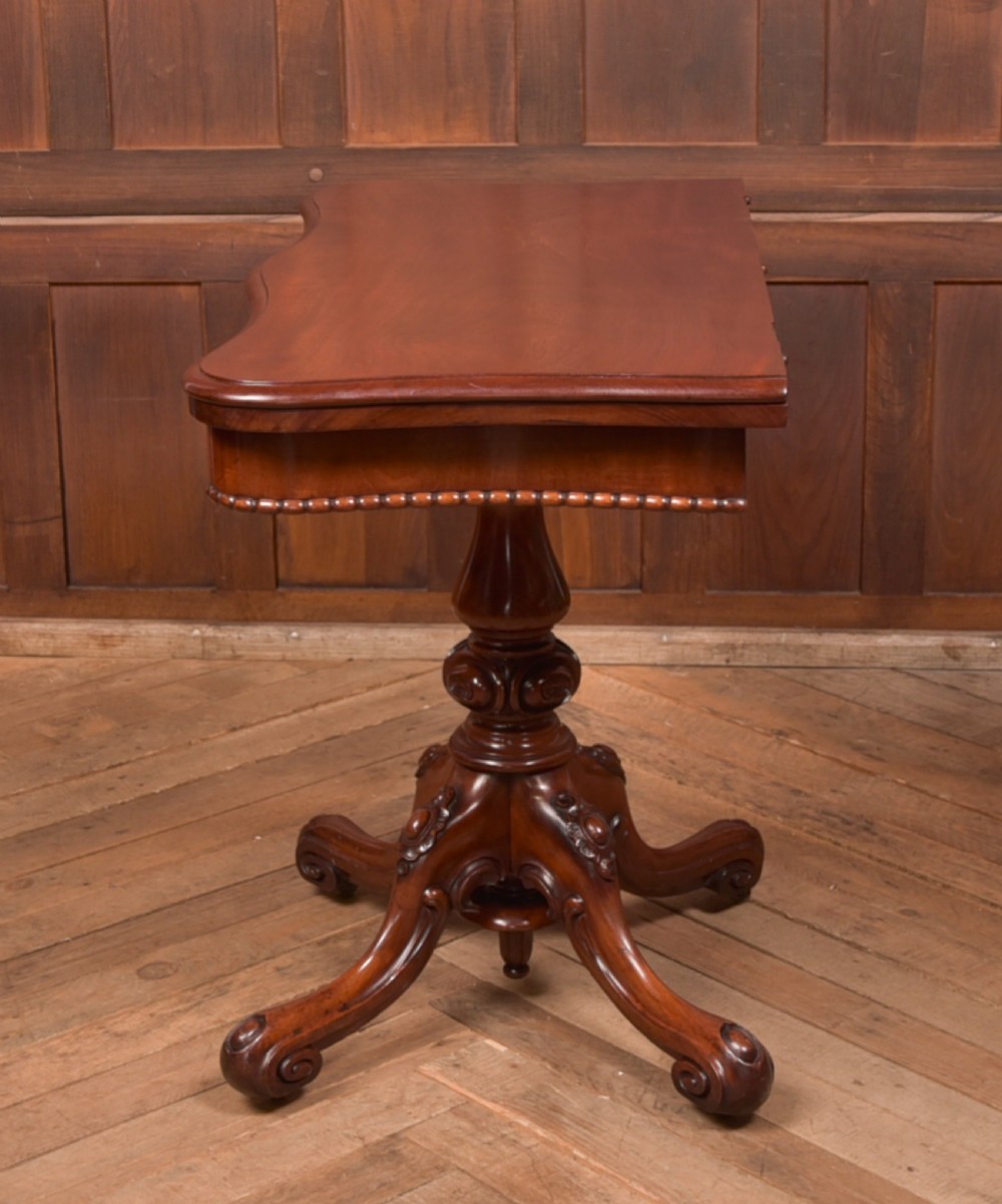 A Victorian mahogany fold-over tea table featuring a serpentine top, bead moulding along the apron, a turned central column, and carved quadruped scroll legs. View XVII