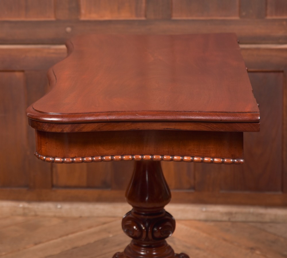 A Victorian mahogany fold-over tea table featuring a serpentine top, bead moulding along the apron, a turned central column, and carved quadruped scroll legs. View XVIII