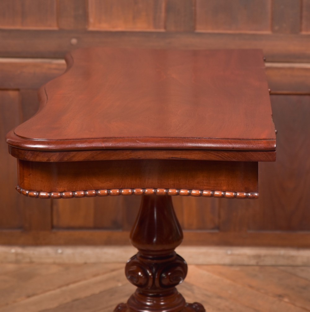 A Victorian mahogany fold-over tea table featuring a serpentine top, bead moulding along the apron, a turned central column, and carved quadruped scroll legs. View XIX