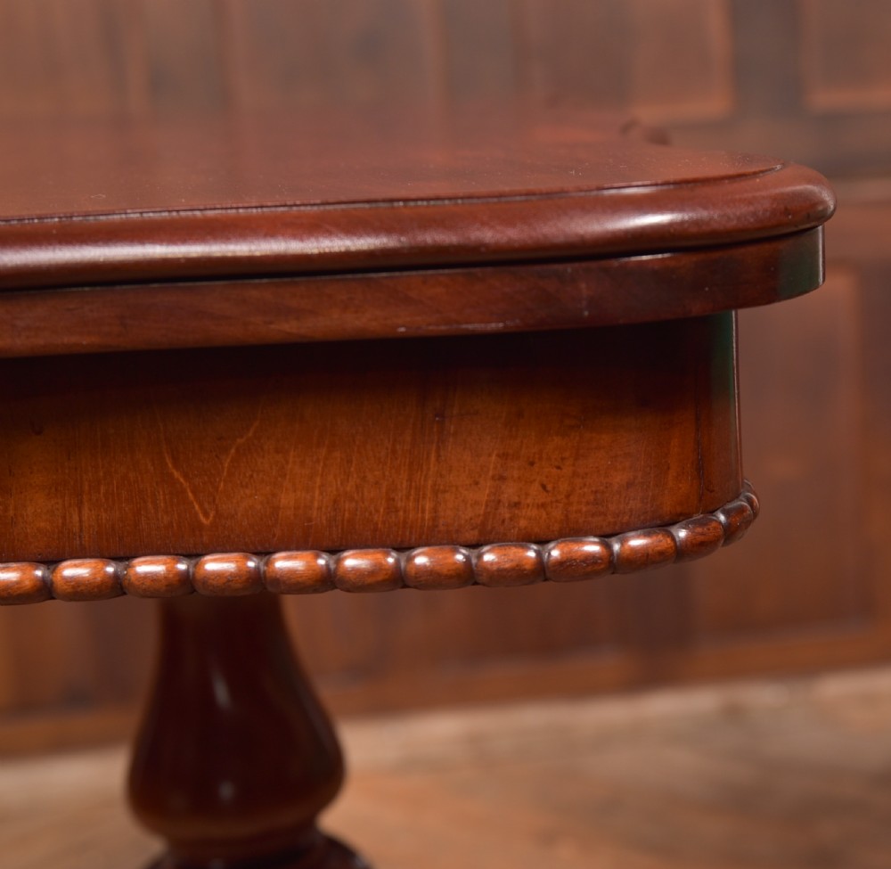 A Victorian mahogany fold-over tea table featuring a serpentine top, bead moulding along the apron, a turned central column, and carved quadruped scroll legs. View XXII