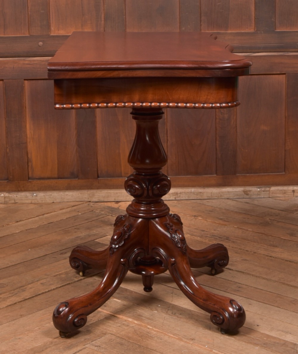 A Victorian mahogany fold-over tea table featuring a serpentine top, bead moulding along the apron, a turned central column, and carved quadruped scroll legs. View XXIV
