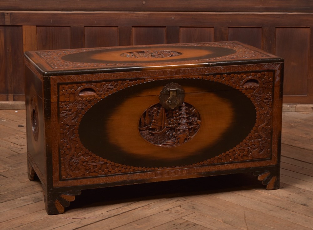 A hand-carved Chinese camphor wood storage chest featuring an oval relief medallion, dragon carvings, and a brass latch plate.