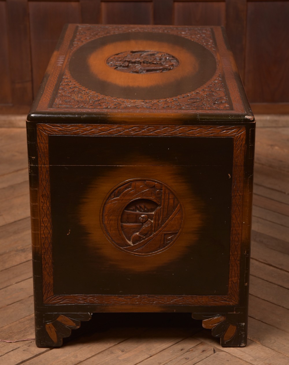 A hand-carved Chinese camphor wood storage chest featuring an oval relief medallion, dragon carvings, and a brass latch plate. View XIV