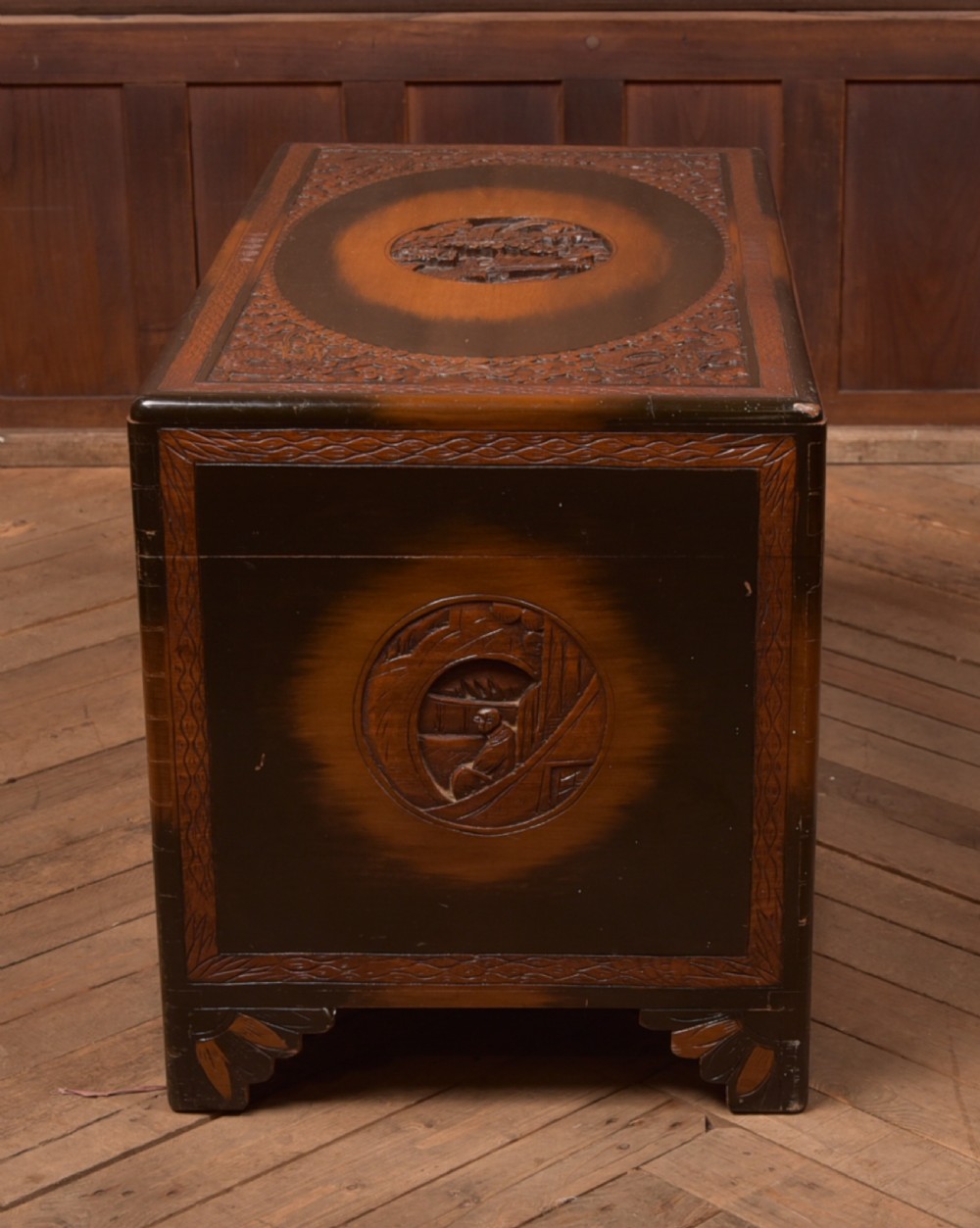 A hand-carved Chinese camphor wood storage chest featuring an oval relief medallion, dragon carvings, and a brass latch plate. View XV