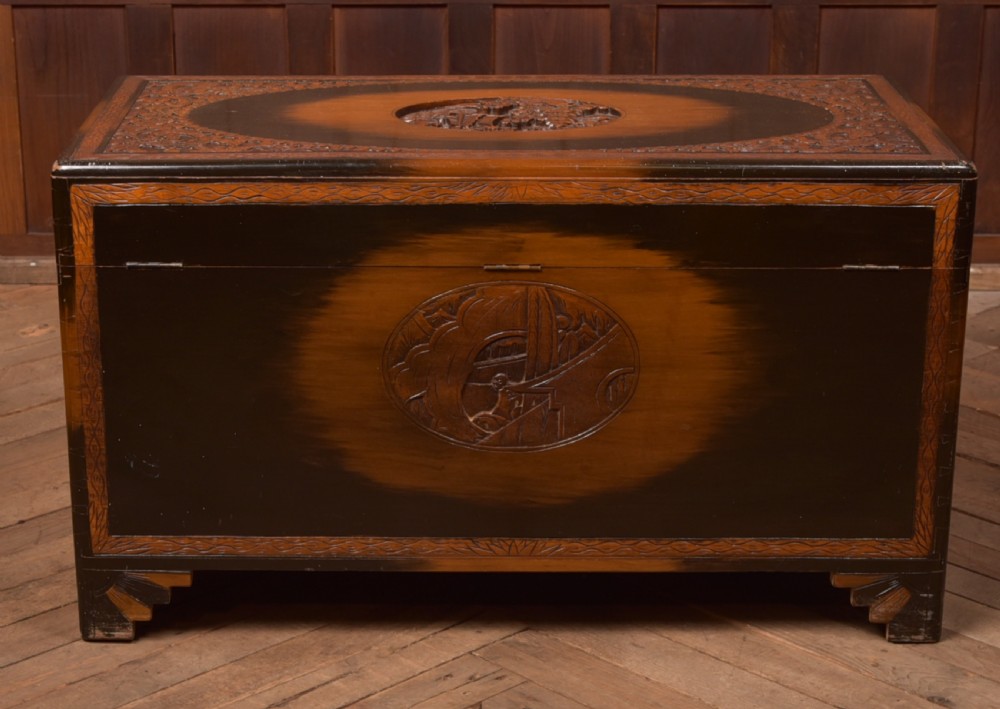 A hand-carved Chinese camphor wood storage chest featuring an oval relief medallion, dragon carvings, and a brass latch plate. View XXI