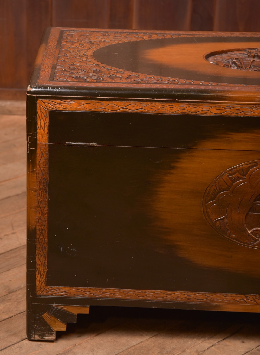 A hand-carved Chinese camphor wood storage chest featuring an oval relief medallion, dragon carvings, and a brass latch plate. View XXII