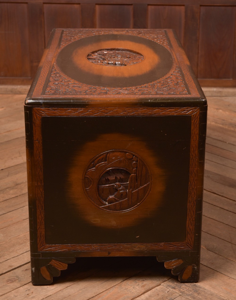 A hand-carved Chinese camphor wood storage chest featuring an oval relief medallion, dragon carvings, and a brass latch plate. View XXIV
