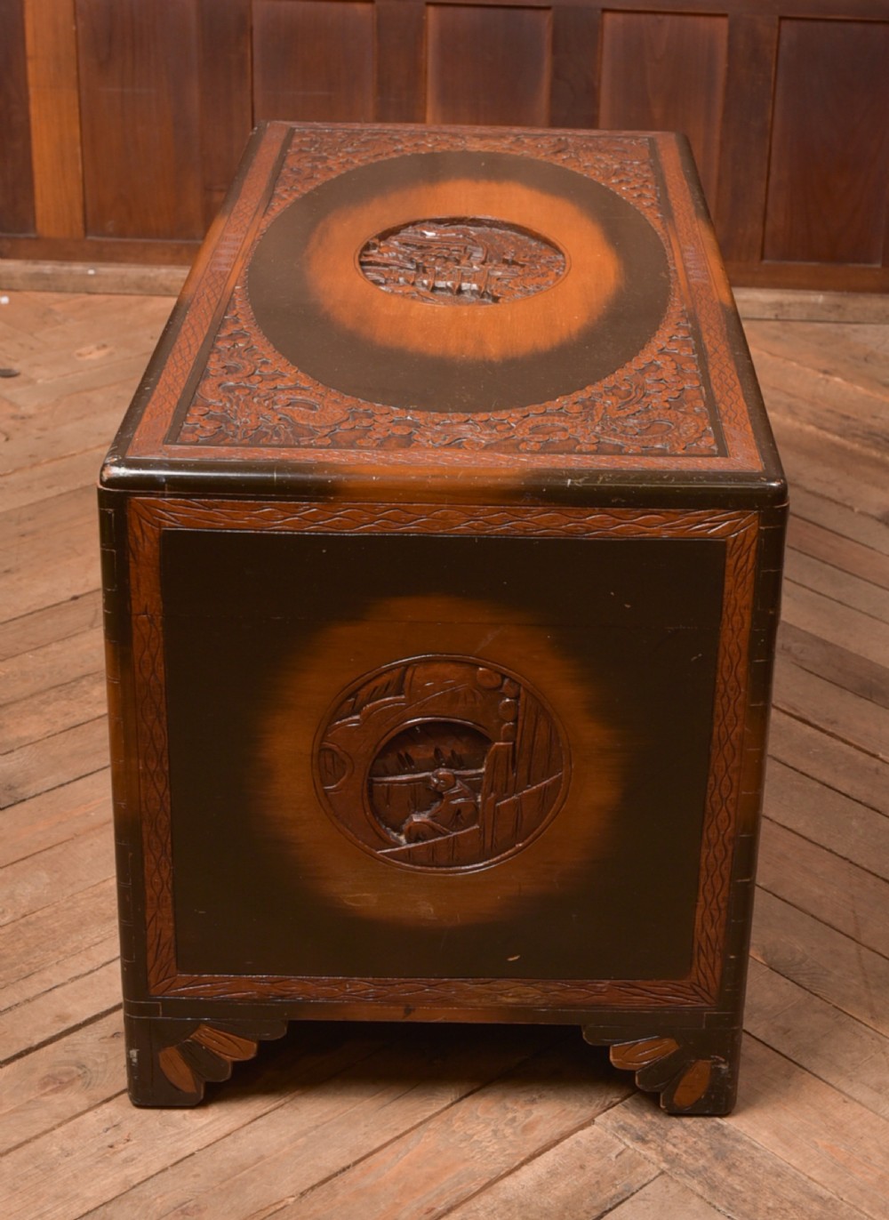 A hand-carved Chinese camphor wood storage chest featuring an oval relief medallion, dragon carvings, and a brass latch plate. View XXV