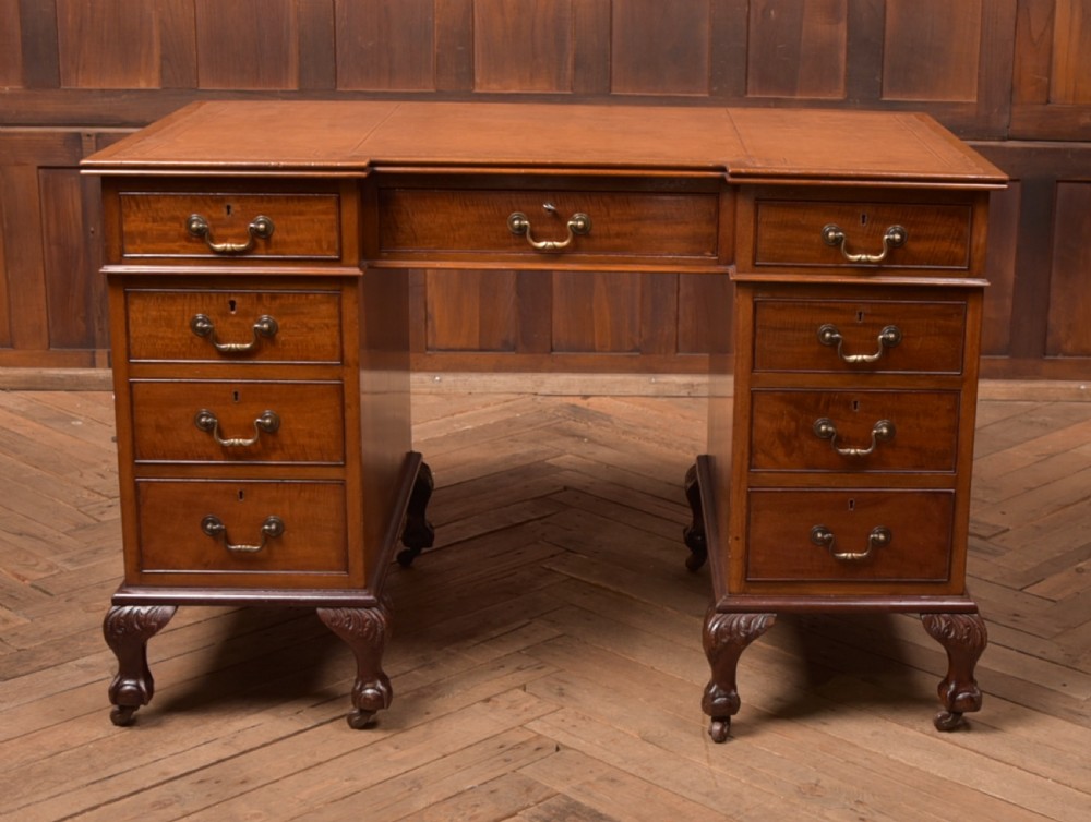 An Edwardian mahogany kneehole writing desk featuring a leather inset top, nine drawers with brass swan neck handles, and carved cabriole legs on ball and claw feet.