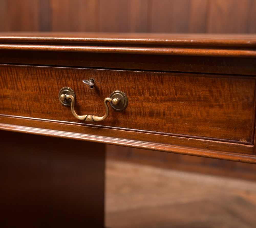 An Edwardian mahogany kneehole writing desk featuring a leather inset top, nine drawers with brass swan neck handles, and carved cabriole legs on ball and claw feet. View VI