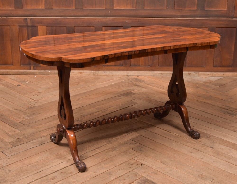 A Victorian rosewood stretcher table featuring a figured top with lobed ends, pierced trestle supports, a barley twist stretcher, and scrolled feet.