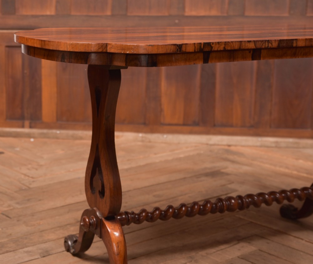 A Victorian rosewood stretcher table featuring a figured top with lobed ends, pierced trestle supports, a barley twist stretcher, and scrolled feet. View II