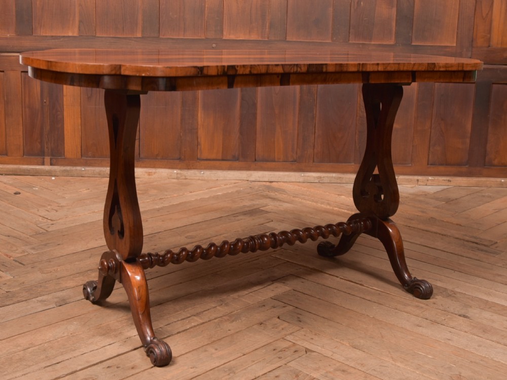 A Victorian rosewood stretcher table featuring a figured top with lobed ends, pierced trestle supports, a barley twist stretcher, and scrolled feet. View III