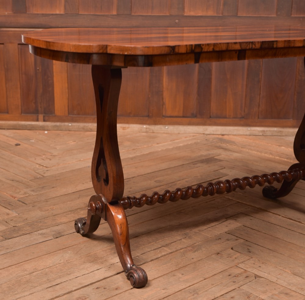 A Victorian rosewood stretcher table featuring a figured top with lobed ends, pierced trestle supports, a barley twist stretcher, and scrolled feet. View V