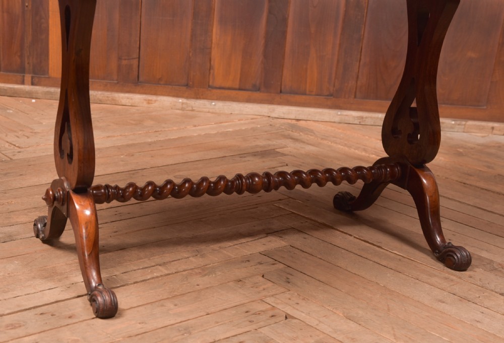 A Victorian rosewood stretcher table featuring a figured top with lobed ends, pierced trestle supports, a barley twist stretcher, and scrolled feet. View VI