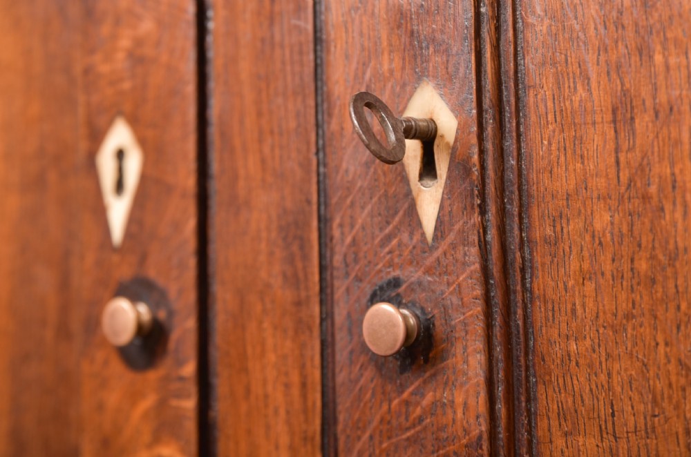 A two-tiered nineteenth-century oak court cupboard featuring panelled doors, drop handles on two upper drawers, and turned finials. View II