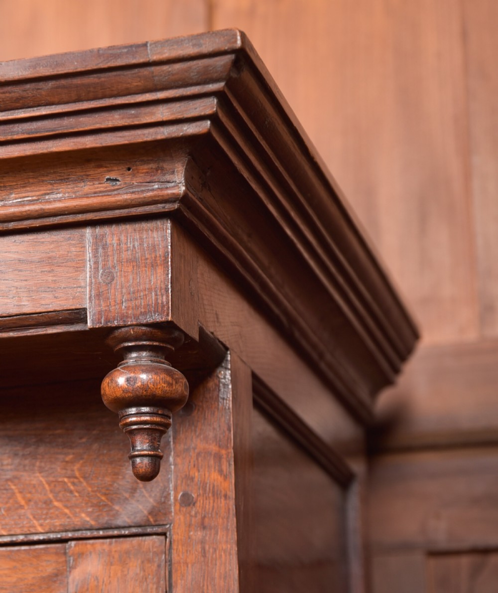 A two-tiered nineteenth-century oak court cupboard featuring panelled doors, drop handles on two upper drawers, and turned finials. View VI