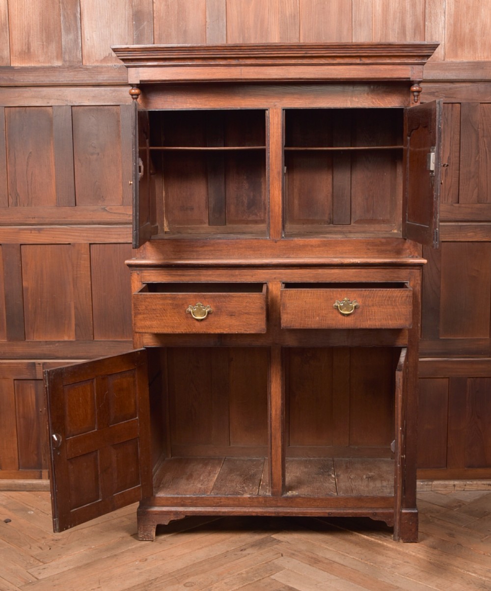 A two-tiered nineteenth-century oak court cupboard featuring panelled doors, drop handles on two upper drawers, and turned finials. View VII