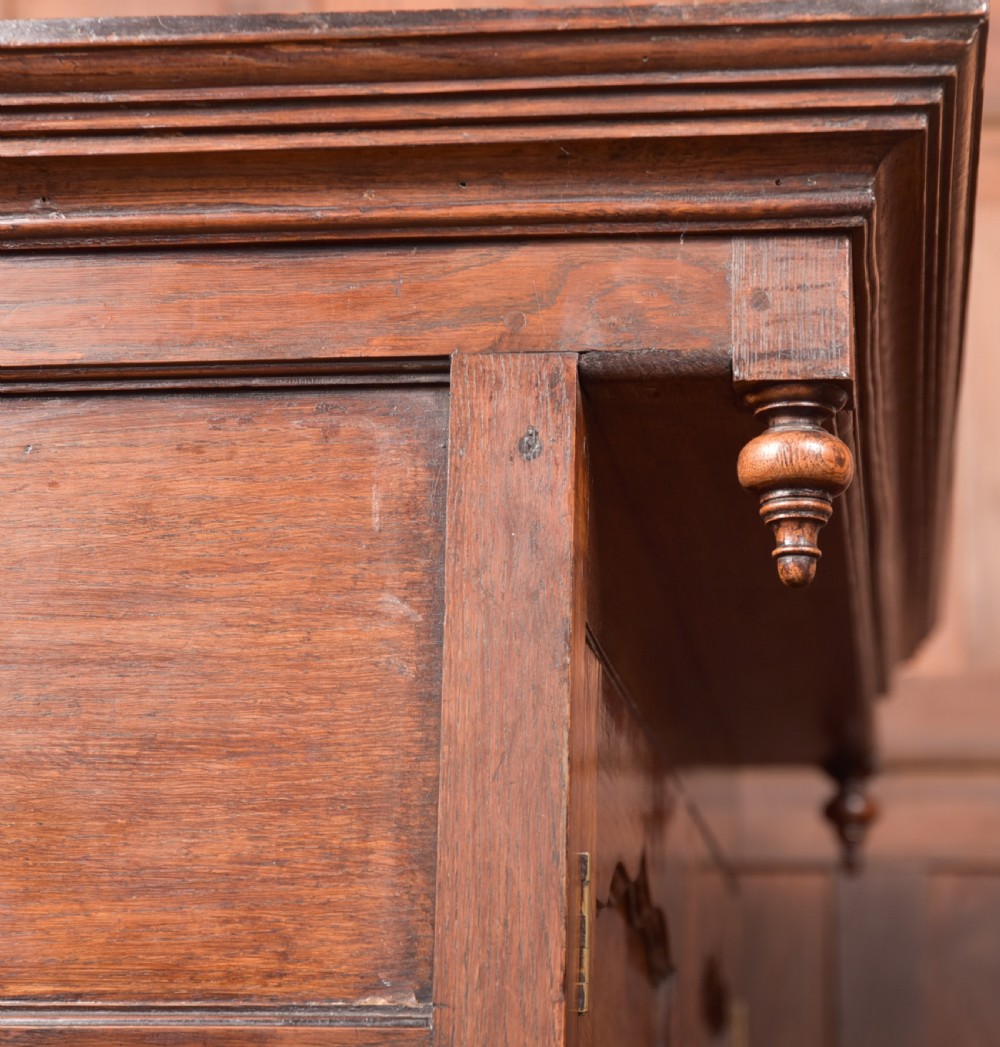 A two-tiered nineteenth-century oak court cupboard featuring panelled doors, drop handles on two upper drawers, and turned finials. View X