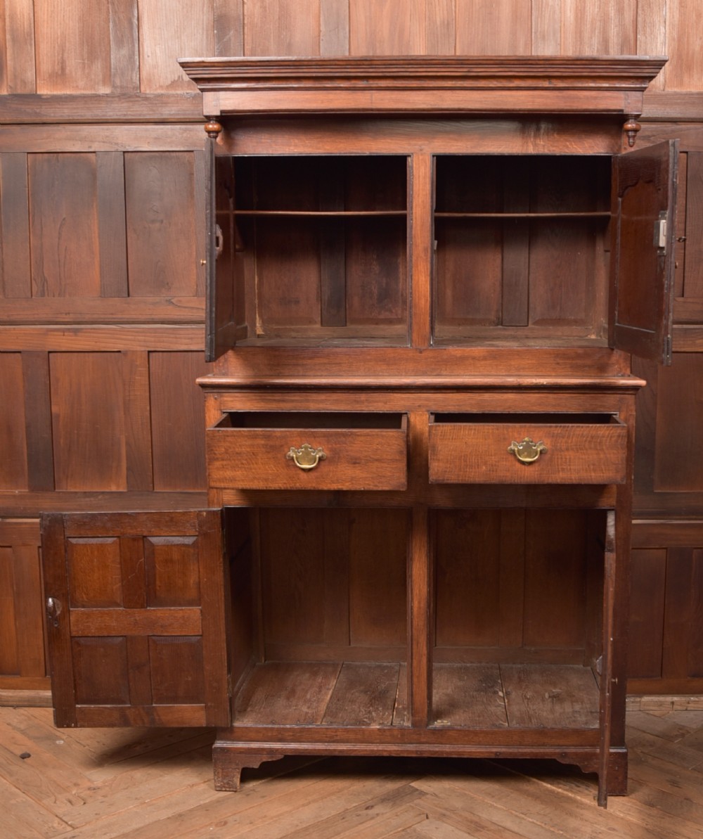 A two-tiered nineteenth-century oak court cupboard featuring panelled doors, drop handles on two upper drawers, and turned finials. View XI